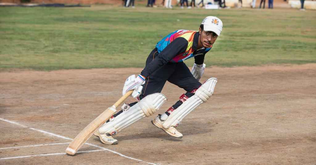 A cricket player in colorful attire bats during a daytime match on a sunny field.